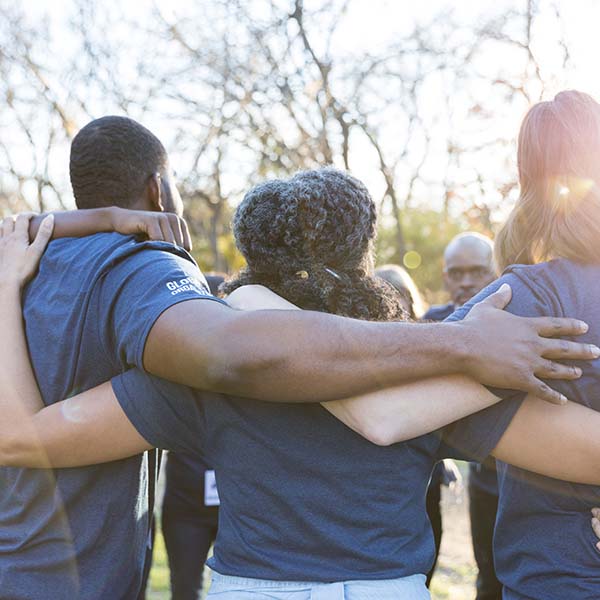 Group of diverse neighbors are unified while participating in a community cleanup event. They are standing with their arms around one another.